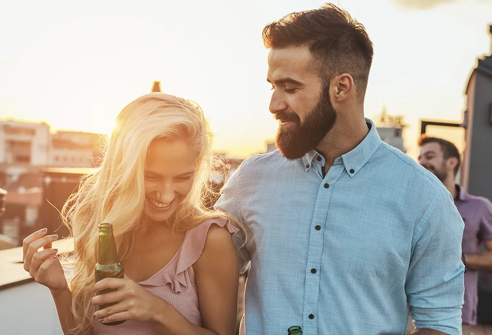 man and woman standing in front of a sunset laughing and enjoying drinks